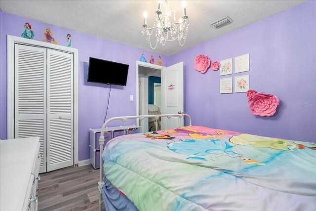 bedroom with visible vents, a closet, wood finished floors, baseboards, and a chandelier