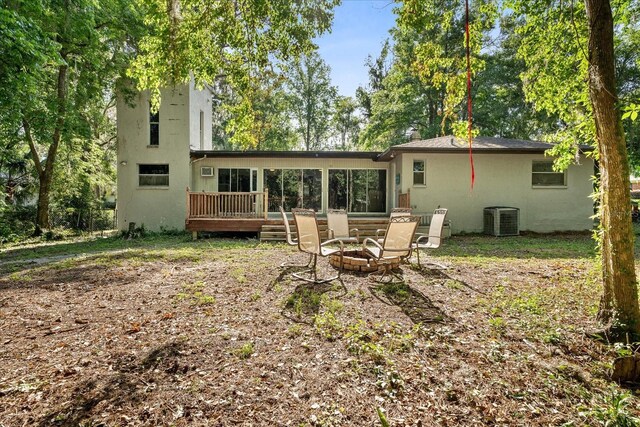 back of property featuring central AC, a deck, stucco siding, a sunroom, and an outdoor fire pit