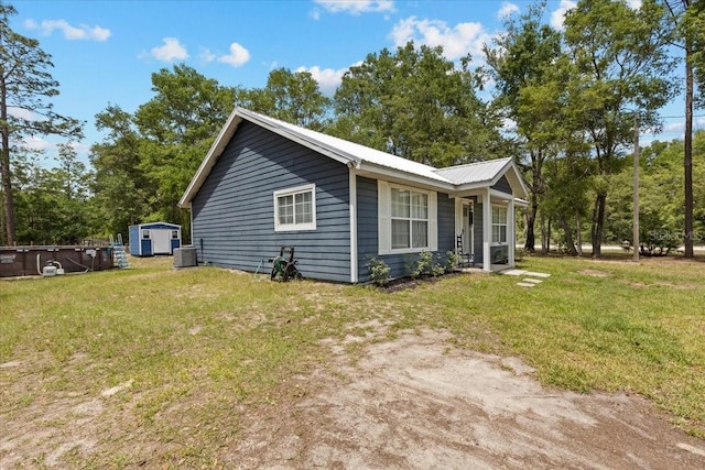 view of side of home featuring central air condition unit, an outbuilding, metal roof, a lawn, and a storage unit