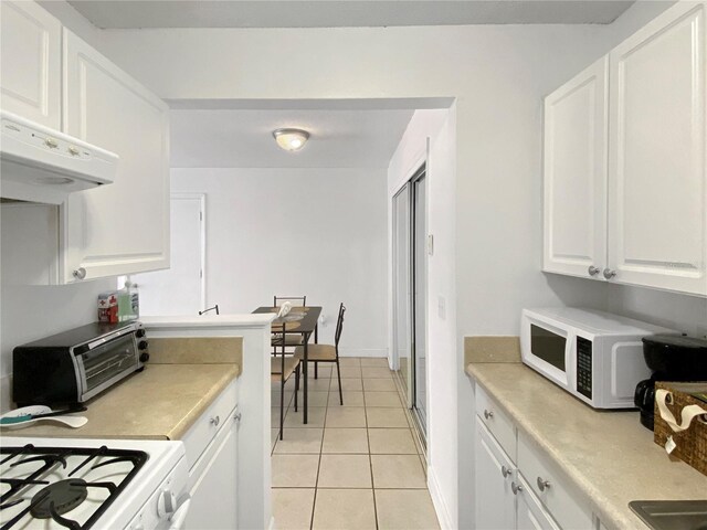 kitchen with range hood, light tile patterned floors, light countertops, white cabinets, and white appliances