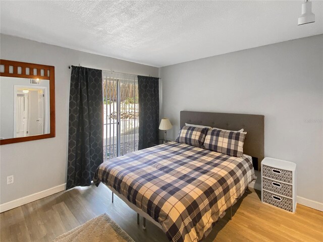 bedroom featuring baseboards, a textured ceiling, and wood finished floors