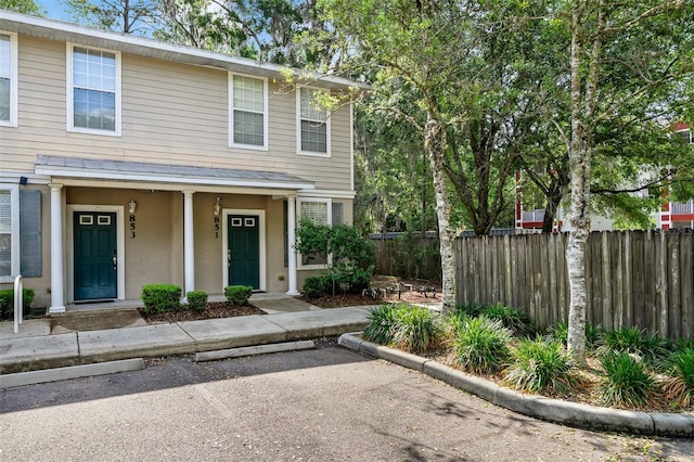 view of front facade with covered porch, fence, uncovered parking, and stucco siding
