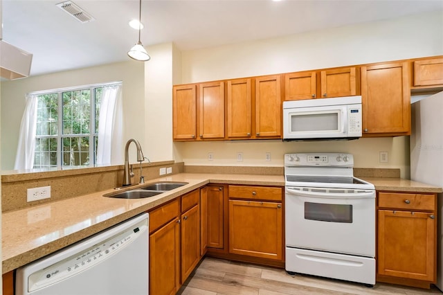 kitchen with brown cabinetry, visible vents, a sink, white appliances, and light wood-style flooring