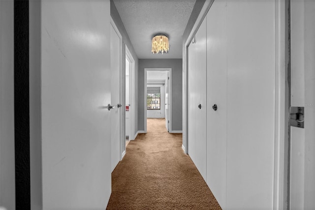 hall featuring baseboards, a chandelier, a textured ceiling, and light colored carpet