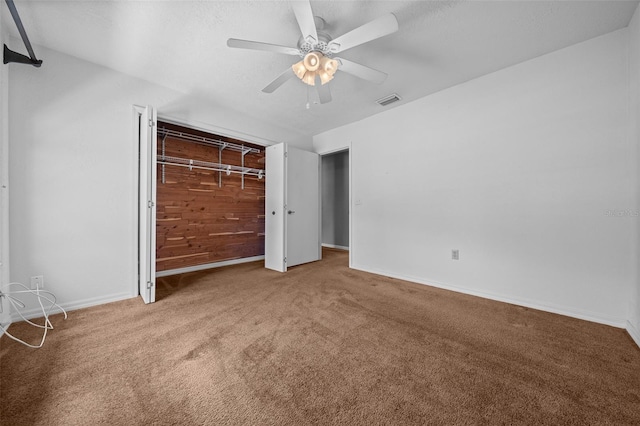 unfurnished bedroom featuring ceiling fan, carpet floors, wood walls, baseboards, and visible vents