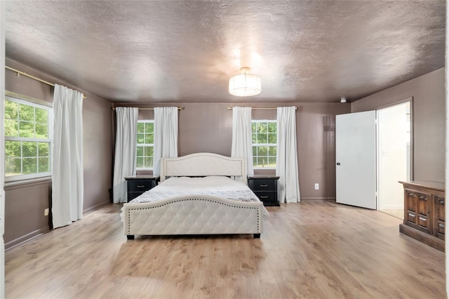 bedroom featuring a textured ceiling, baseboards, multiple windows, and light wood-style floors