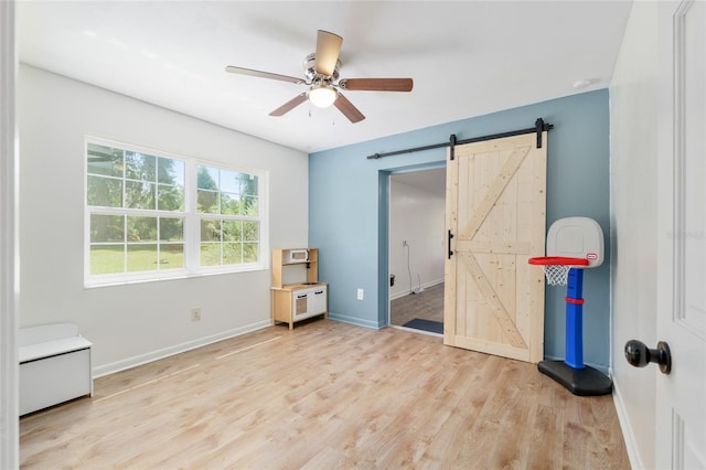 unfurnished bedroom with a ceiling fan, baseboards, a barn door, and light wood-style floors