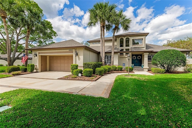 view of front facade with a garage, a front lawn, stucco siding, a shingled roof, and driveway