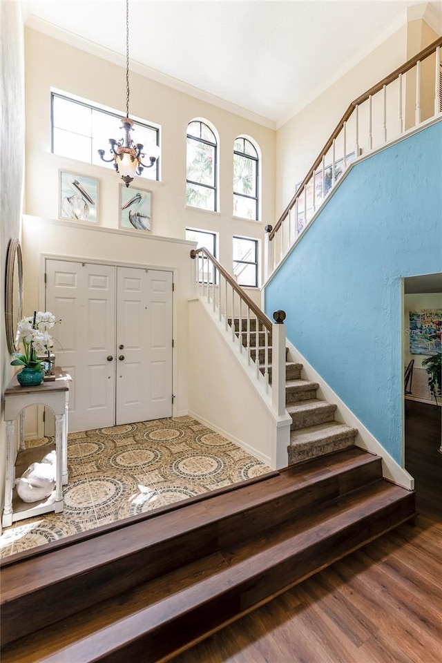 foyer with wood finished floors, a high ceiling, an inviting chandelier, ornamental molding, and stairs