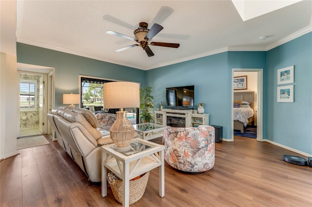living area with ornamental molding, wood finished floors, baseboards, ceiling fan, and a skylight