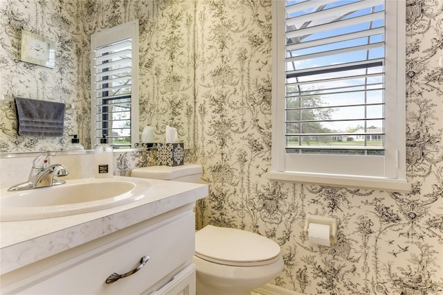 half bath with toilet, wallpapered walls, and vanity