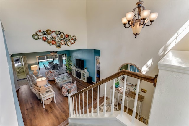 stairway featuring a notable chandelier, wood finished floors, and a towering ceiling