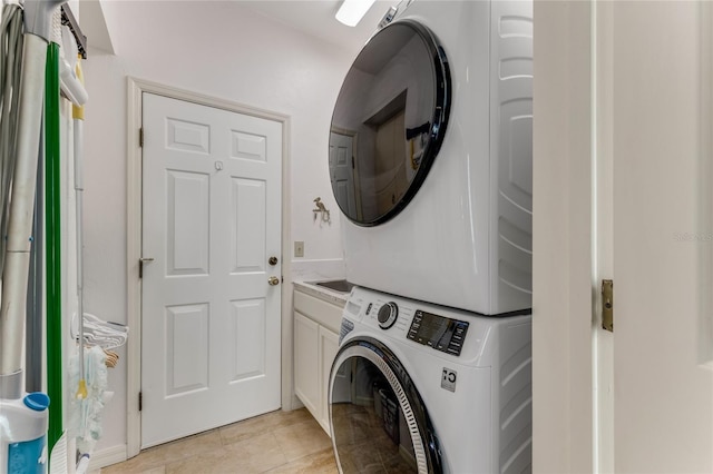 laundry area with cabinet space, light tile patterned flooring, and stacked washer / dryer