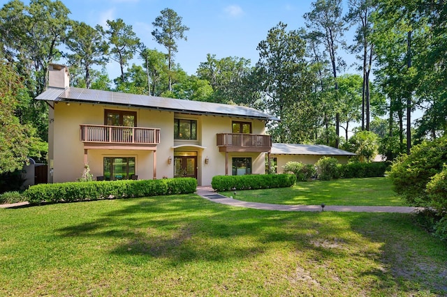 view of front facade featuring stucco siding, a front yard, a chimney, a balcony, and french doors
