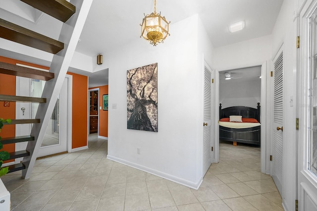 corridor featuring light tile patterned floors, baseboards, and stairs