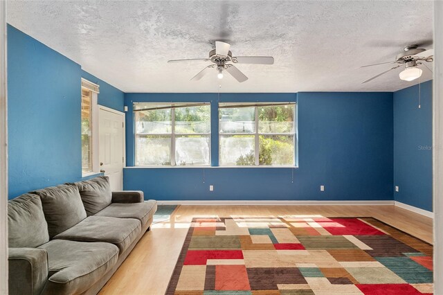 living room featuring baseboards, a textured ceiling, ceiling fan, and wood finished floors