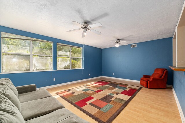 sitting room with a ceiling fan, a textured ceiling, visible vents, and wood finished floors