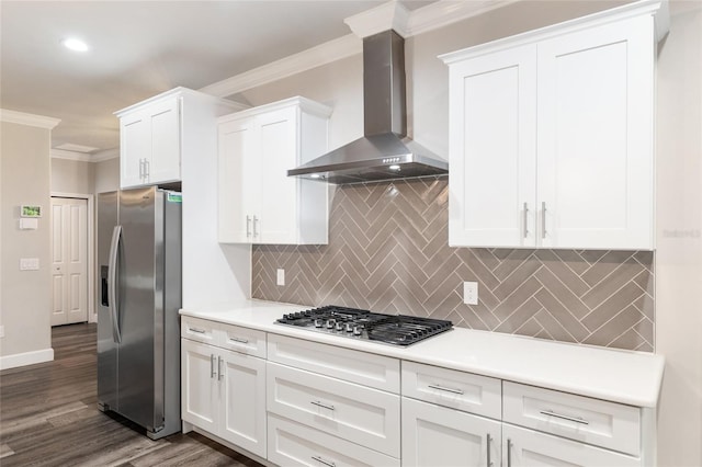 kitchen featuring wall chimney range hood, white cabinets, appliances with stainless steel finishes, light countertops, and ornamental molding