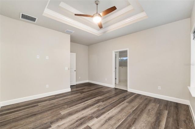 empty room with visible vents, dark wood finished floors, crown molding, and a tray ceiling