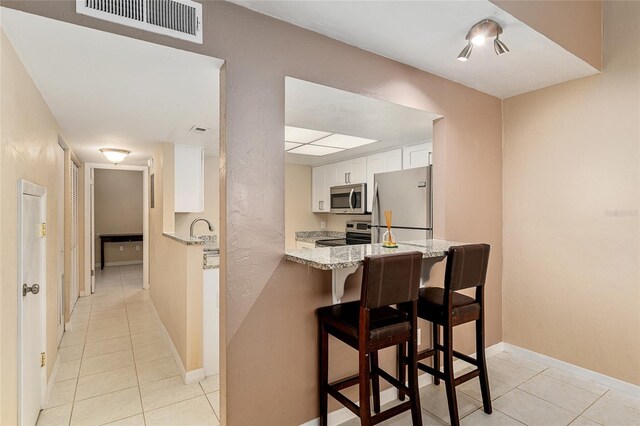kitchen with light tile patterned flooring, appliances with stainless steel finishes, light stone counters, white cabinetry, and visible vents