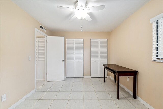unfurnished bedroom featuring light tile patterned flooring, ceiling fan, multiple closets, baseboards, and visible vents