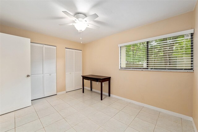 unfurnished bedroom featuring light tile patterned floors, multiple closets, baseboards, and a ceiling fan