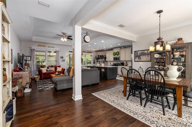 dining room with crown molding, ceiling fan with notable chandelier, dark wood-type flooring, and visible vents