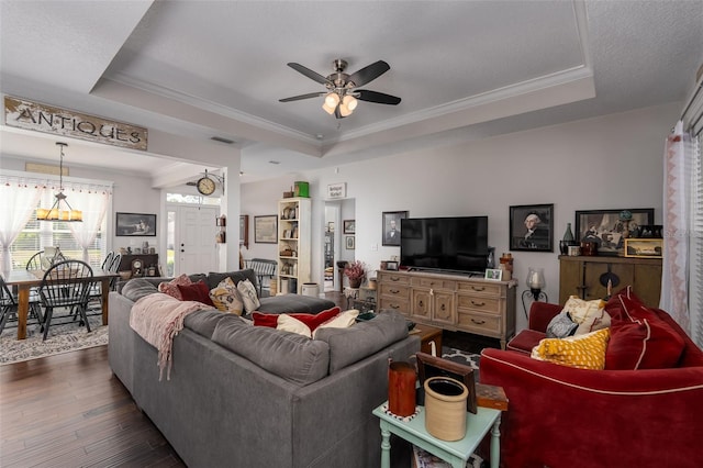 living area with visible vents, ornamental molding, dark wood-style flooring, a tray ceiling, and a ceiling fan