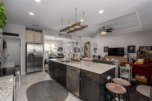 kitchen featuring a ceiling fan, appliances with stainless steel finishes, a center island with sink, a sink, and open floor plan