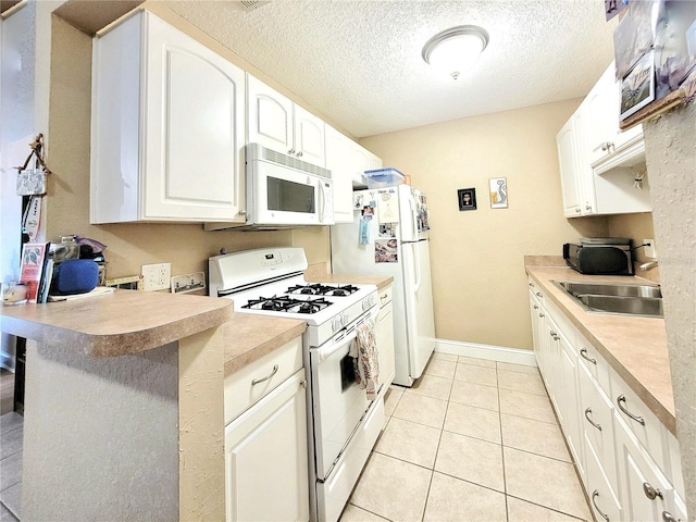 kitchen with white appliances, a sink, a peninsula, a textured ceiling, and white cabinets