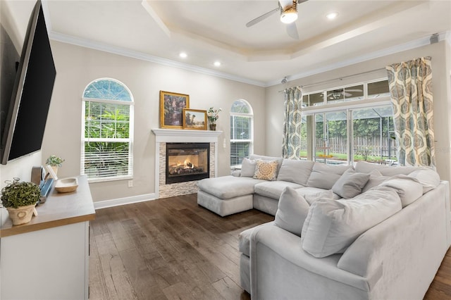 living room with a ceiling fan, a glass covered fireplace, a tray ceiling, recessed lighting, and dark wood-type flooring