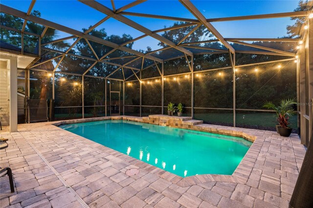 pool at night featuring glass enclosure, a patio area, and an outdoor pool