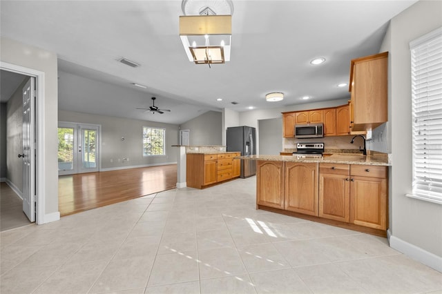 kitchen featuring appliances with stainless steel finishes, a sink, a peninsula, open floor plan, and vaulted ceiling
