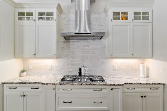 kitchen featuring wall chimney range hood, white cabinetry, stainless steel gas cooktop, and decorative backsplash
