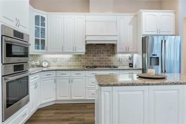 4515 SW 97th Ter, Gainesville, FL 32608 - kitchen with appliances with stainless steel finishes, glass insert cabinets, white cabinets, light stone countertops, and custom exhaust hood