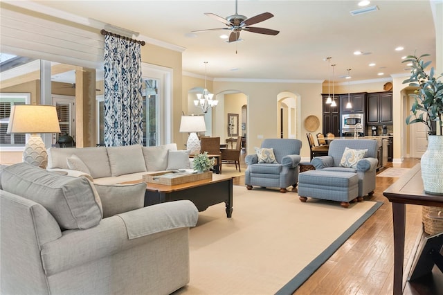living room with arched walkways, a ceiling fan, light wood-style floors, ornamental molding, and recessed lighting