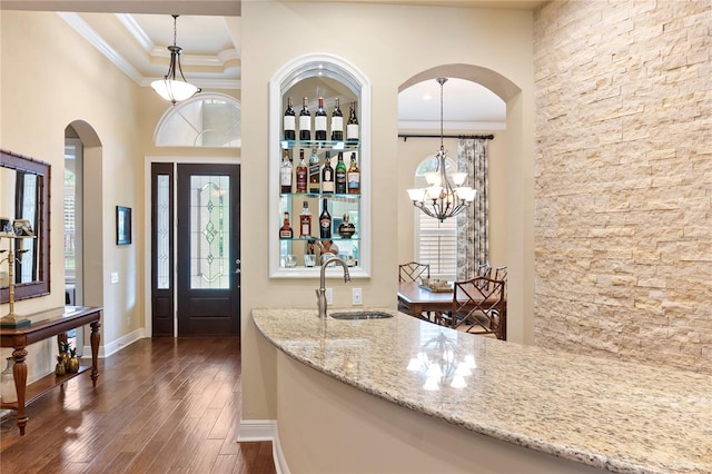 foyer entrance featuring ornamental molding, dark wood-type flooring, arched walkways, a chandelier, and baseboards