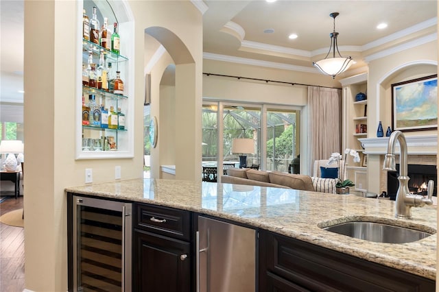 kitchen with wine cooler, a sink, crown molding, plenty of natural light, and light stone countertops