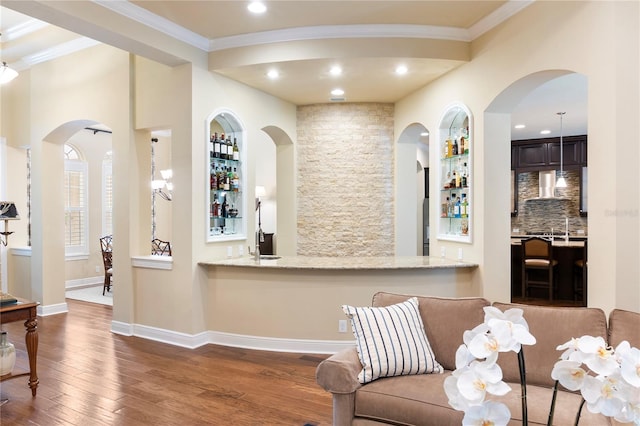 interior space featuring wood finished floors, wall chimney exhaust hood, crown molding, light stone counters, and recessed lighting