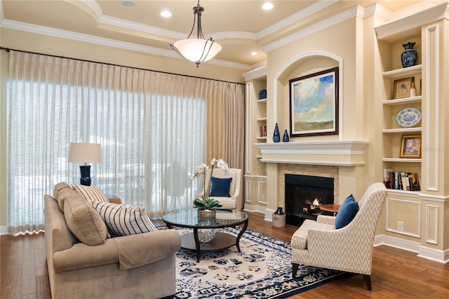 living area featuring wood finished floors, a tile fireplace, built in features, and ornamental molding