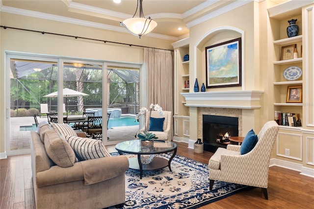 living area with built in features, wood finished floors, ornamental molding, a glass covered fireplace, and a sunroom