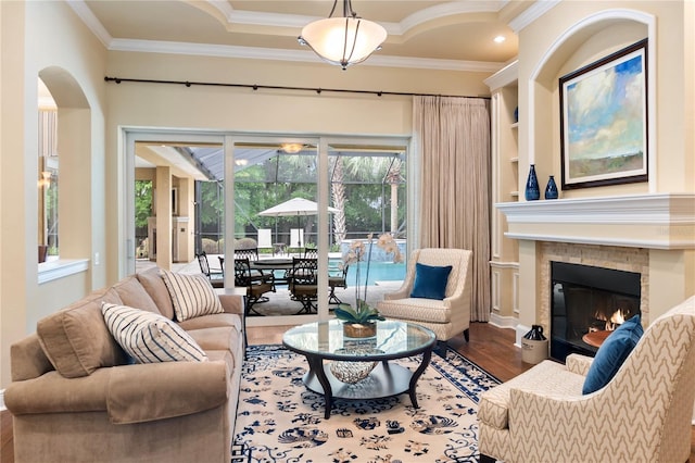 living room featuring wood finished floors, ornamental molding, a stone fireplace, arched walkways, and built in features