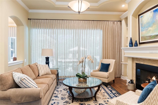 living area featuring wood finished floors, ornamental molding, a tile fireplace, and arched walkways