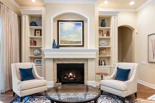 sitting room with built in features, wood finished floors, baseboards, a fireplace with flush hearth, and ornamental molding