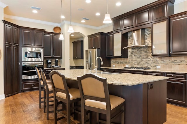 kitchen with appliances with stainless steel finishes, wall chimney range hood, crown molding, a sink, and decorative backsplash