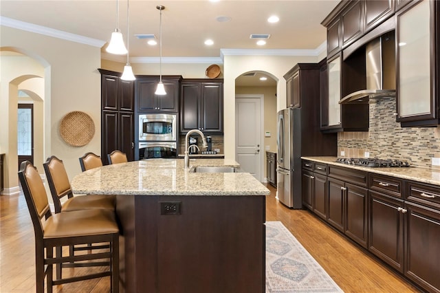 kitchen featuring stainless steel appliances, wall chimney exhaust hood, arched walkways, a breakfast bar area, and a sink