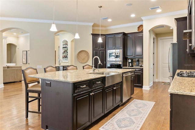 kitchen with a breakfast bar, a sink, appliances with stainless steel finishes, arched walkways, and an island with sink