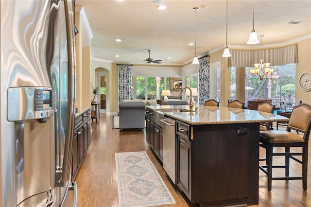 kitchen featuring stainless steel appliances, a kitchen breakfast bar, arched walkways, a sink, and crown molding