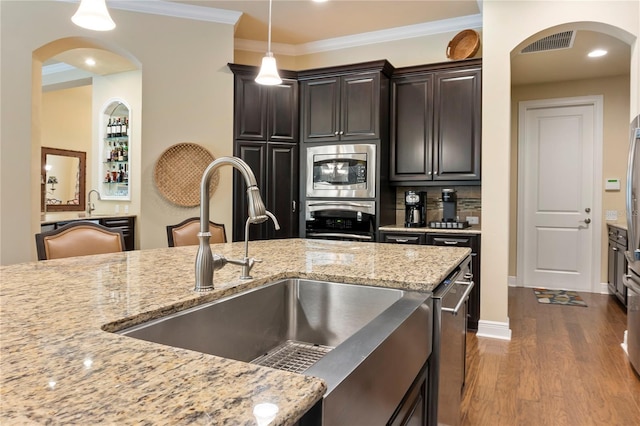 kitchen with a sink, stainless steel appliances, arched walkways, hanging light fixtures, and wood finished floors
