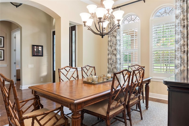 dining area featuring wood finished floors, arched walkways, a chandelier, and baseboards